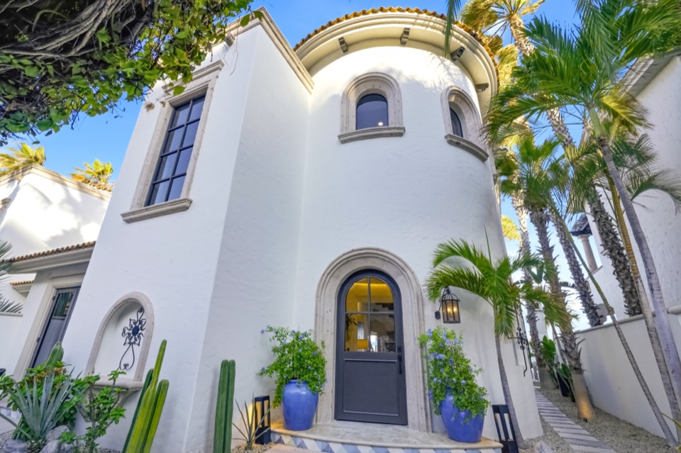 The rounded stucco turret and arched entry of the villa, framed by palms and Talavera pottery
