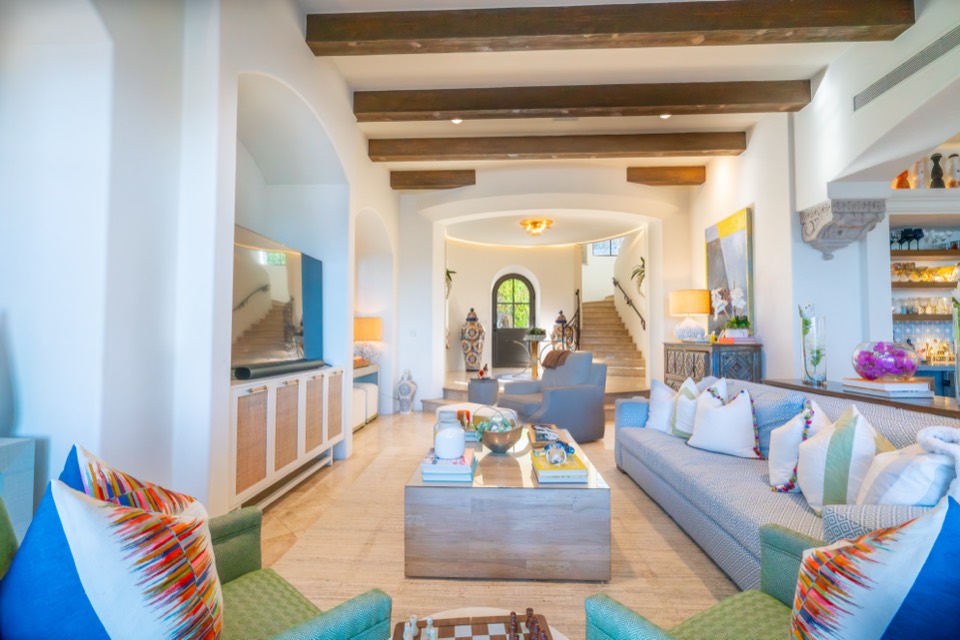 The great room with wood-beamed ceilings, a curved staircase and travertine floors