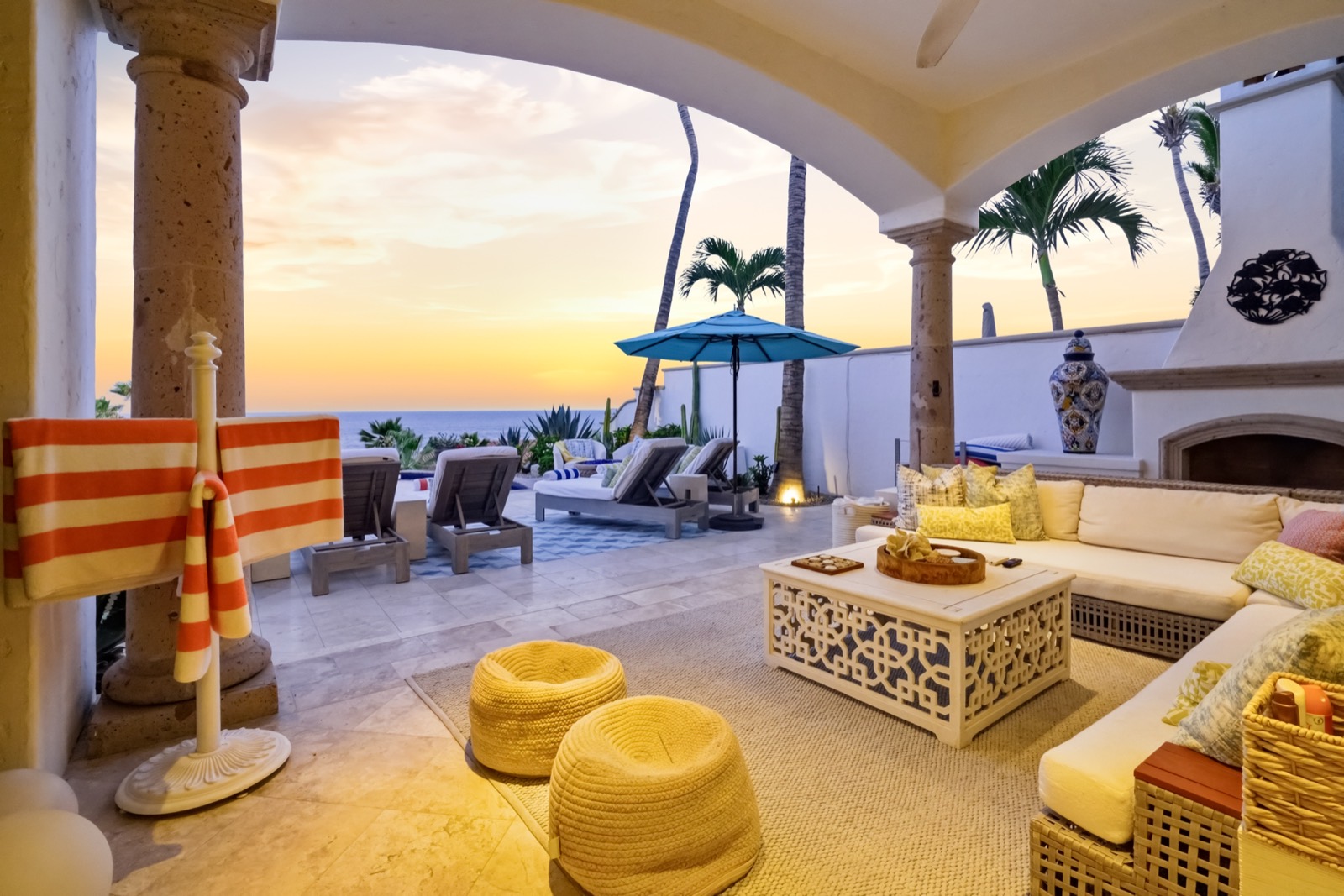 A covered terrace lounge at golden hour, the sun low over the water